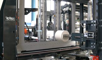 Die von Koch Robotersysteme integrierte Verpackungslinie führt Rollen per robotergesteuertem Spanndorngreifer durch die RoRo StretchPack-Verpackungsmaschine von Tentoma (Quelle: Tentoma)